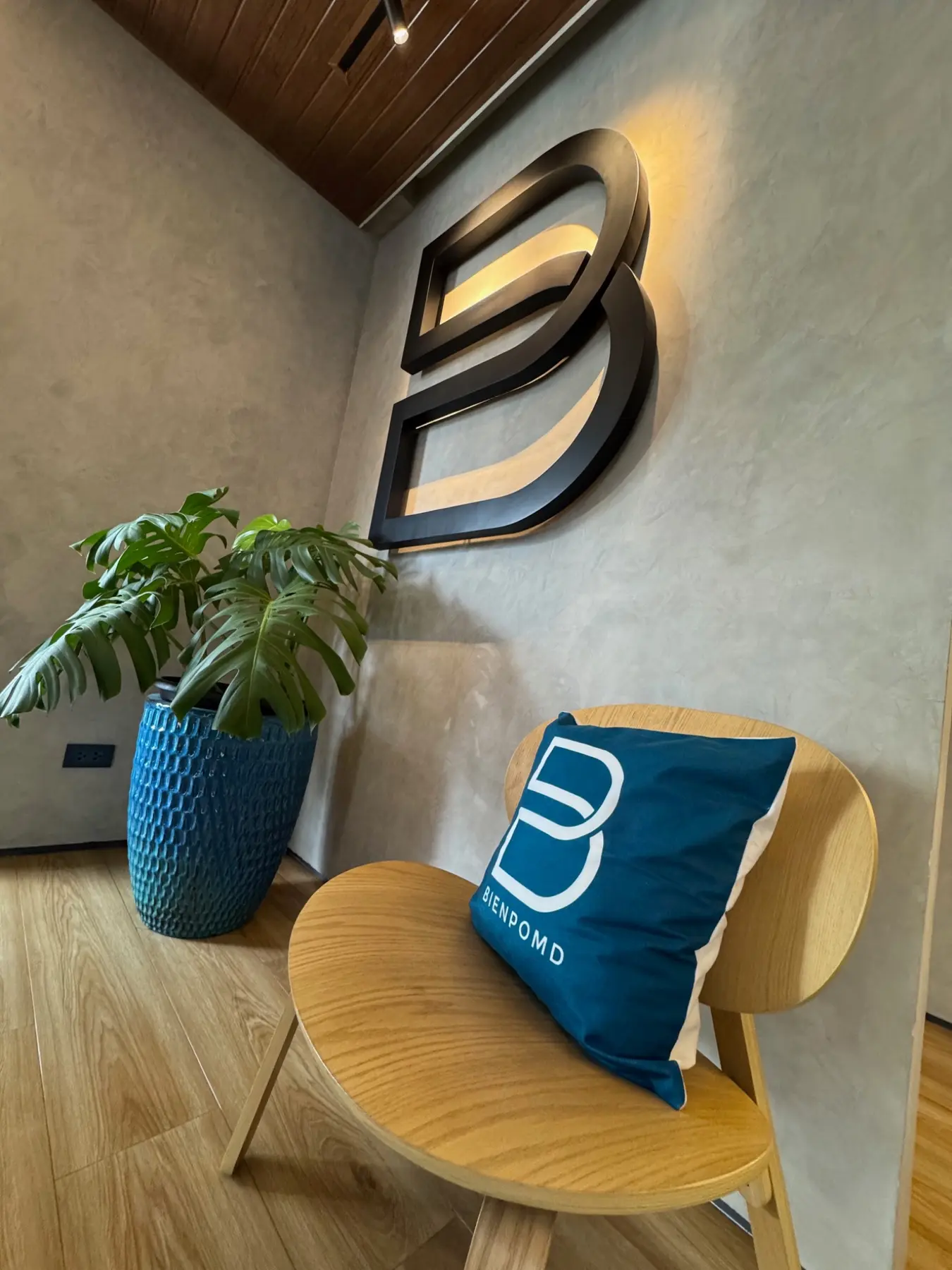 BienPoMD Aesthetics logo wall with plant and wooden waiting chair
